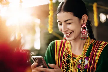 7000 BDT App — Fast, responsive, and optimized for all devices A cheerful woman in traditional clothing using her smartphone during a festive moment, showing how easily the 7000 BDT app fits into everyday life.